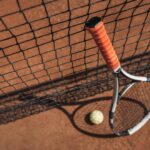 close-up shot of tennis ball and racket leaning on net