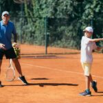 Tennis Instructor with Boy Having a Tennis Lesson on Clay Court.